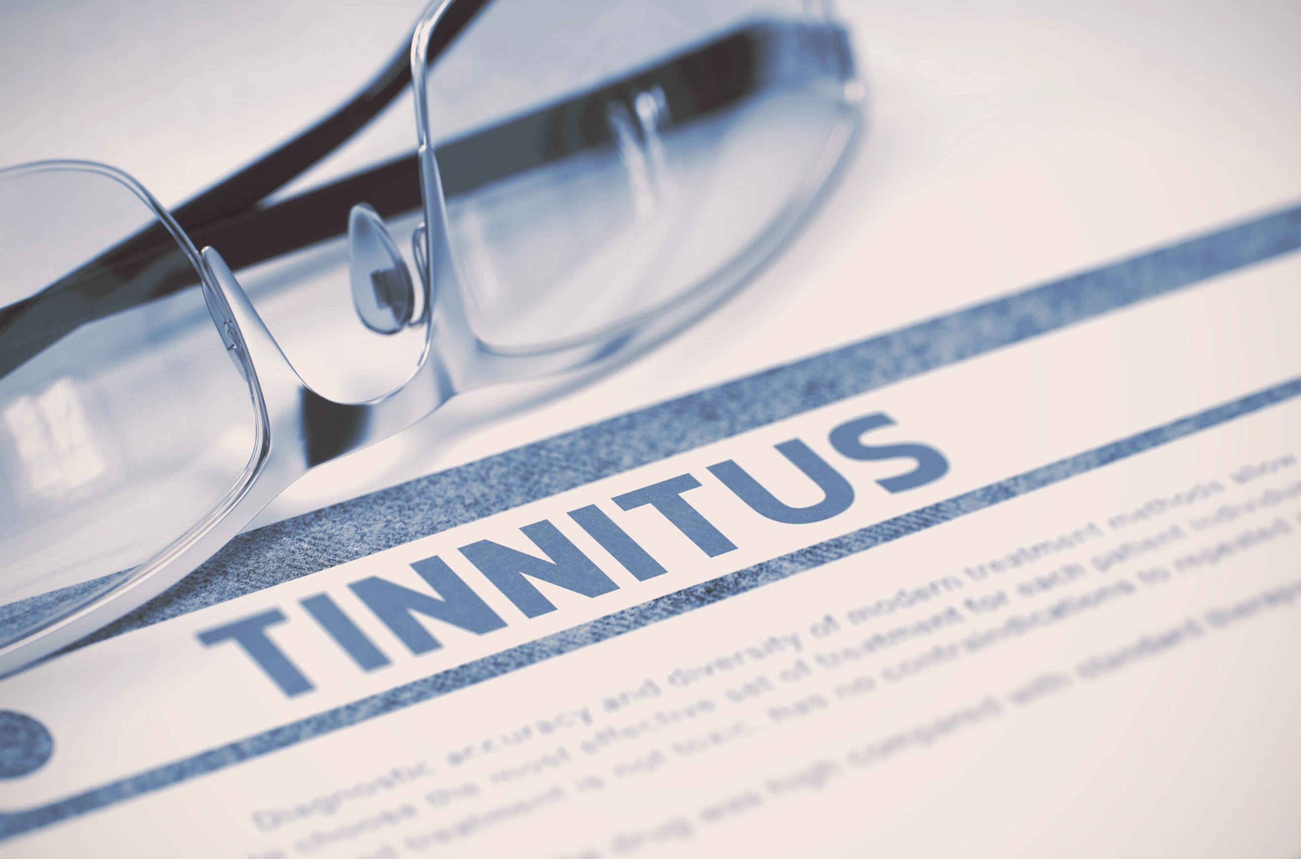 A close-up of eyeglasses resting on a document with the word "Tinnitus" prominently displayed in bold blue letters, representing medical or informational content related to tinnitus.